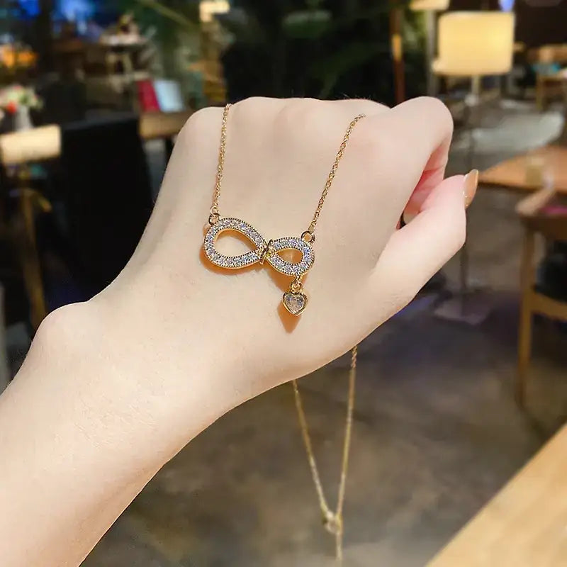 Gold infinity symbol necklace adorned with sparkling clear stones and a dangling heart charm.