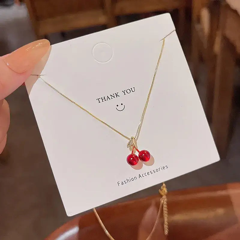 A delicate gold chain necklace featuring two glossy red cherry pendants.