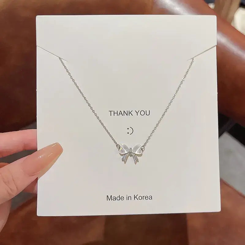 A delicate silver necklace featuring a sparkling bow pendant, displayed on a white card.