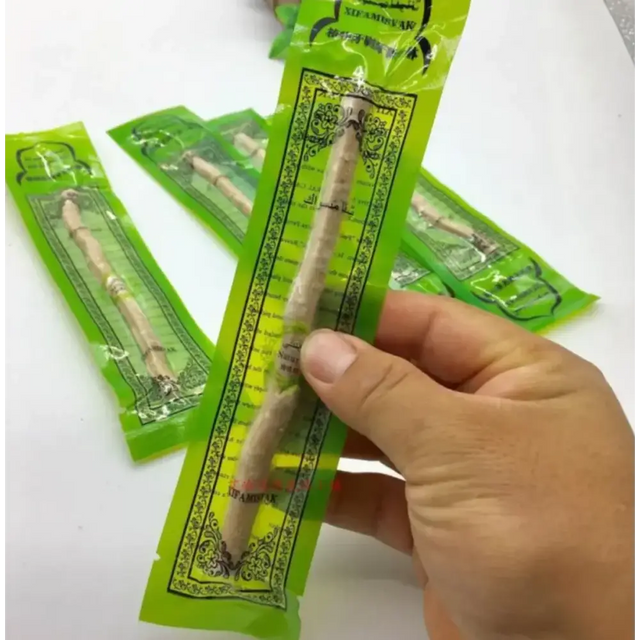 A hand holds a single green-packaged stick of licorice root, branded as ’sedamak’ with arabic script and ornate black border design.