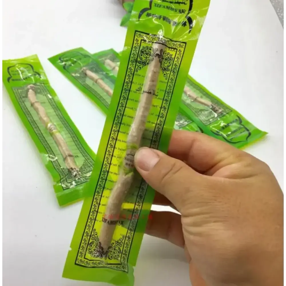 A hand holds a single green-packaged stick of licorice root, branded as ’sedamak’ with arabic script and ornate black border design.