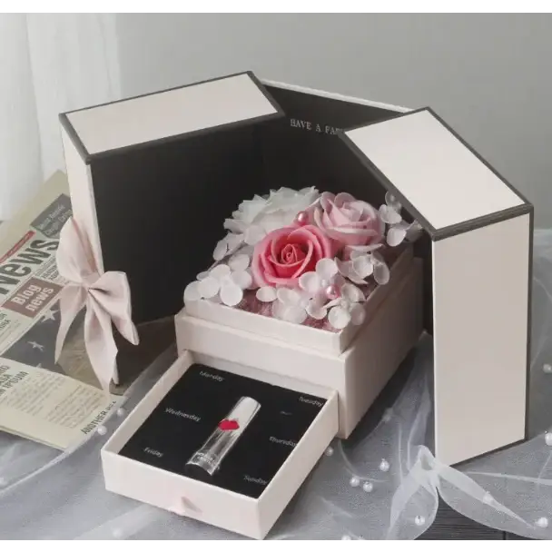 A delicate cream-colored box with a hinged lid, containing an arrangement of pink and white preserved roses surrounded by small pearl-like embellishments.