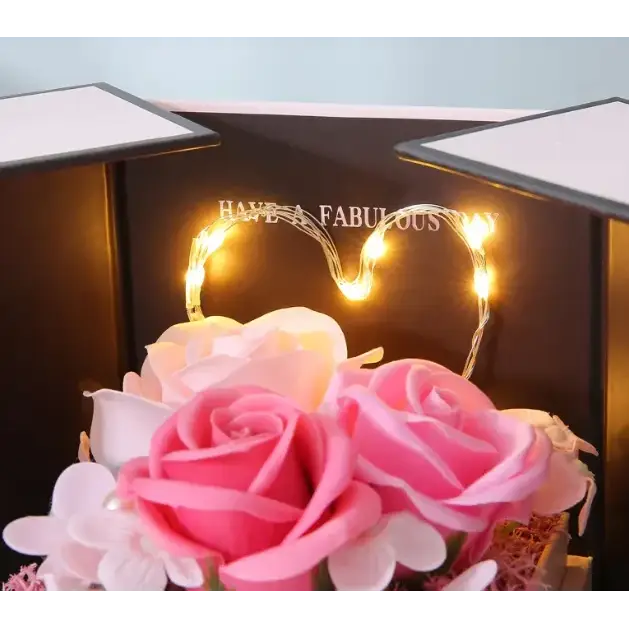 A heart-shaped string of warm white led lights rests above a bouquet of pink and cream-colored artificial roses.