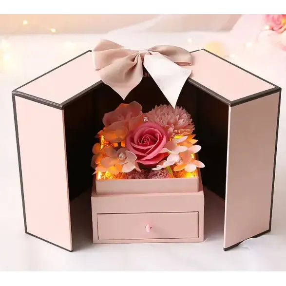 Pink hexagonal box with a beige bow, containing preserved flowers and warm interior lighting.