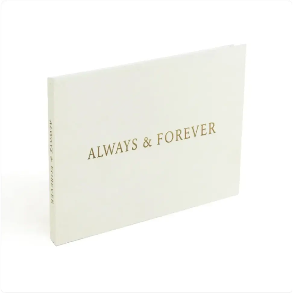 A minimalist white photo album with elegant gold foil lettering that reads ’always & forever’ on the cover.