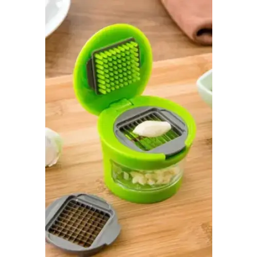 Green plastic garlic press with a clear glass base and interchangeable metal grater attachments.