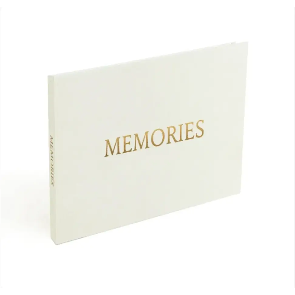 A sleek white memory book with elegant gold foil lettering spelling ’memories’ on the cover.