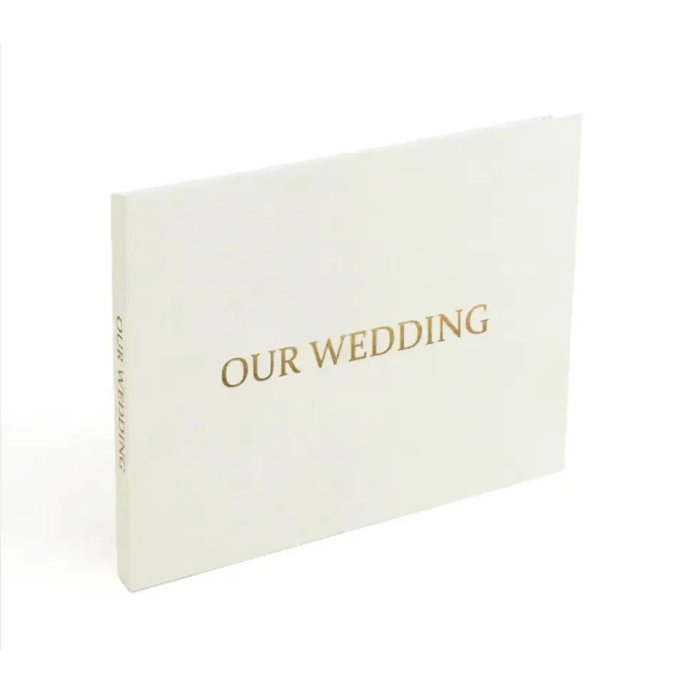 A minimalist white wedding photo album with elegant gold foil lettering that reads ’our wedding’ on the cover.