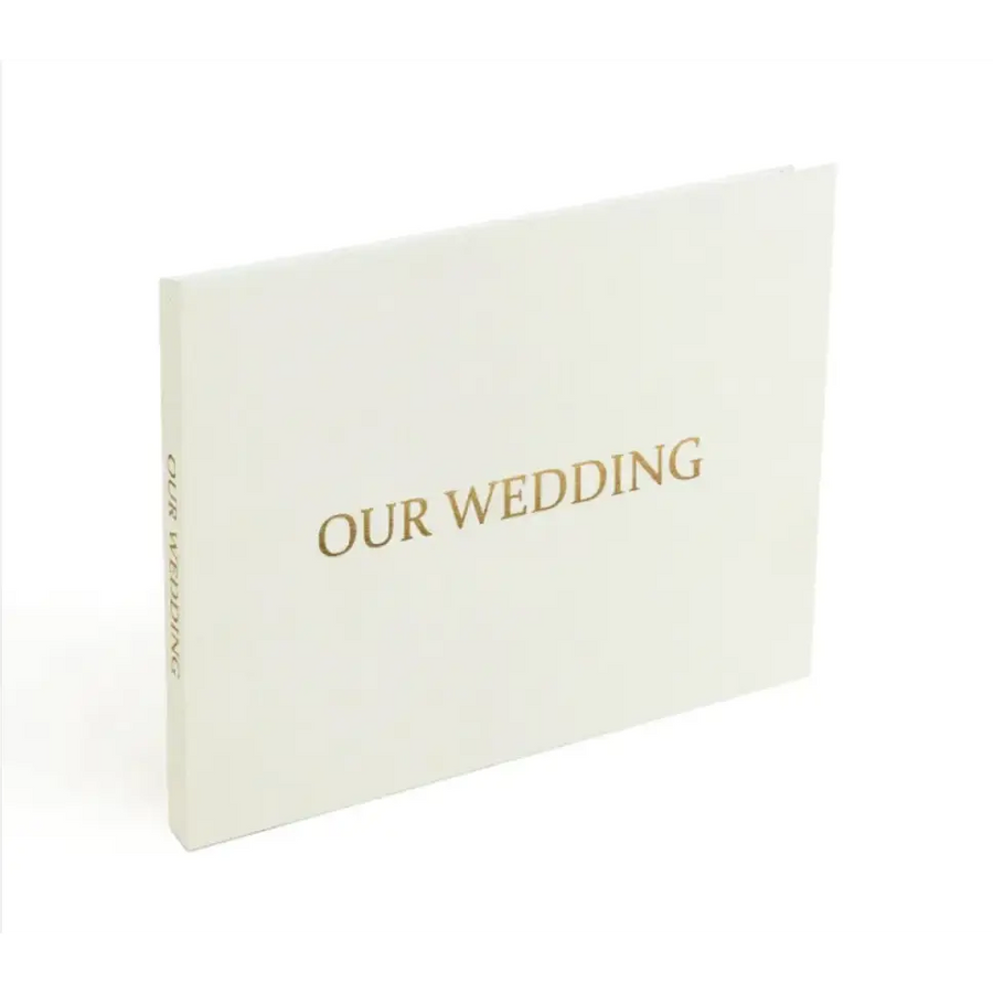 A minimalist white wedding photo album with elegant gold foil lettering that reads ’our wedding’ on the cover.
