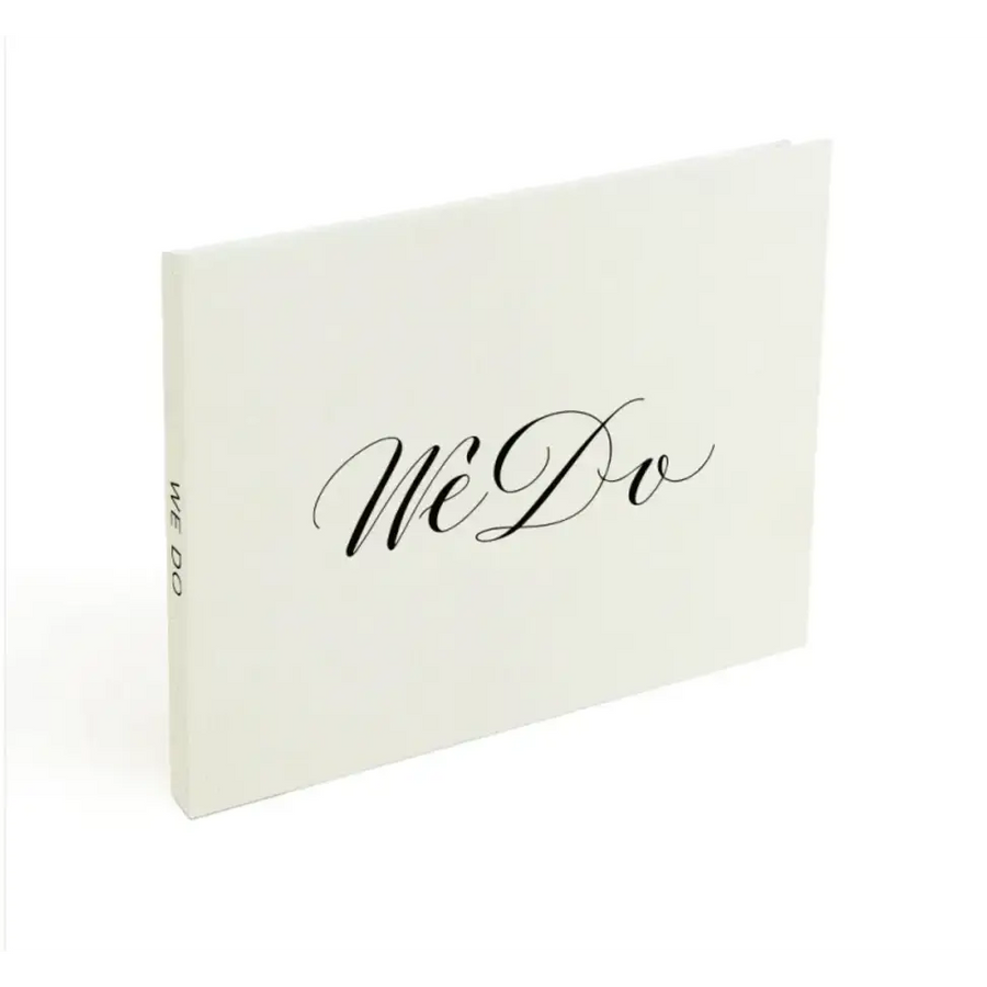 Cream-colored wedding photo album with elegant black cursive ’we do’ lettering on the cover.