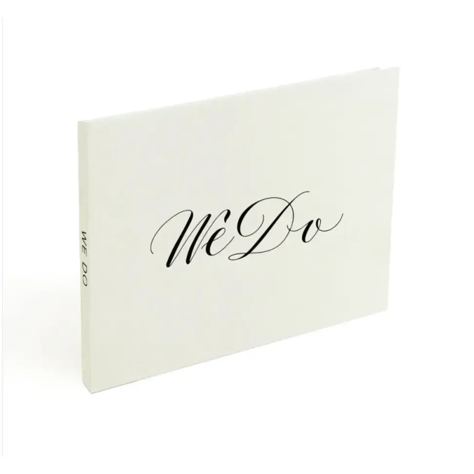 Cream-colored wedding photo album with elegant black cursive ’we do’ lettering on the cover.