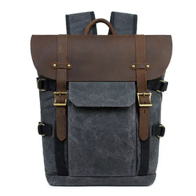 Dark gray canvas backpack with brown leather accents and gold-tone buckles.