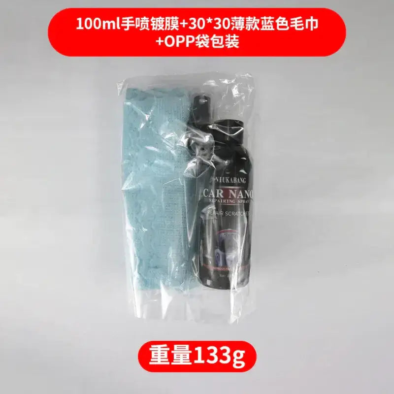Black spray bottle labeled ’niukabang car nano repairing spray’ sits beside a light blue microfiber cloth, both enclosed in clear plastic packaging.