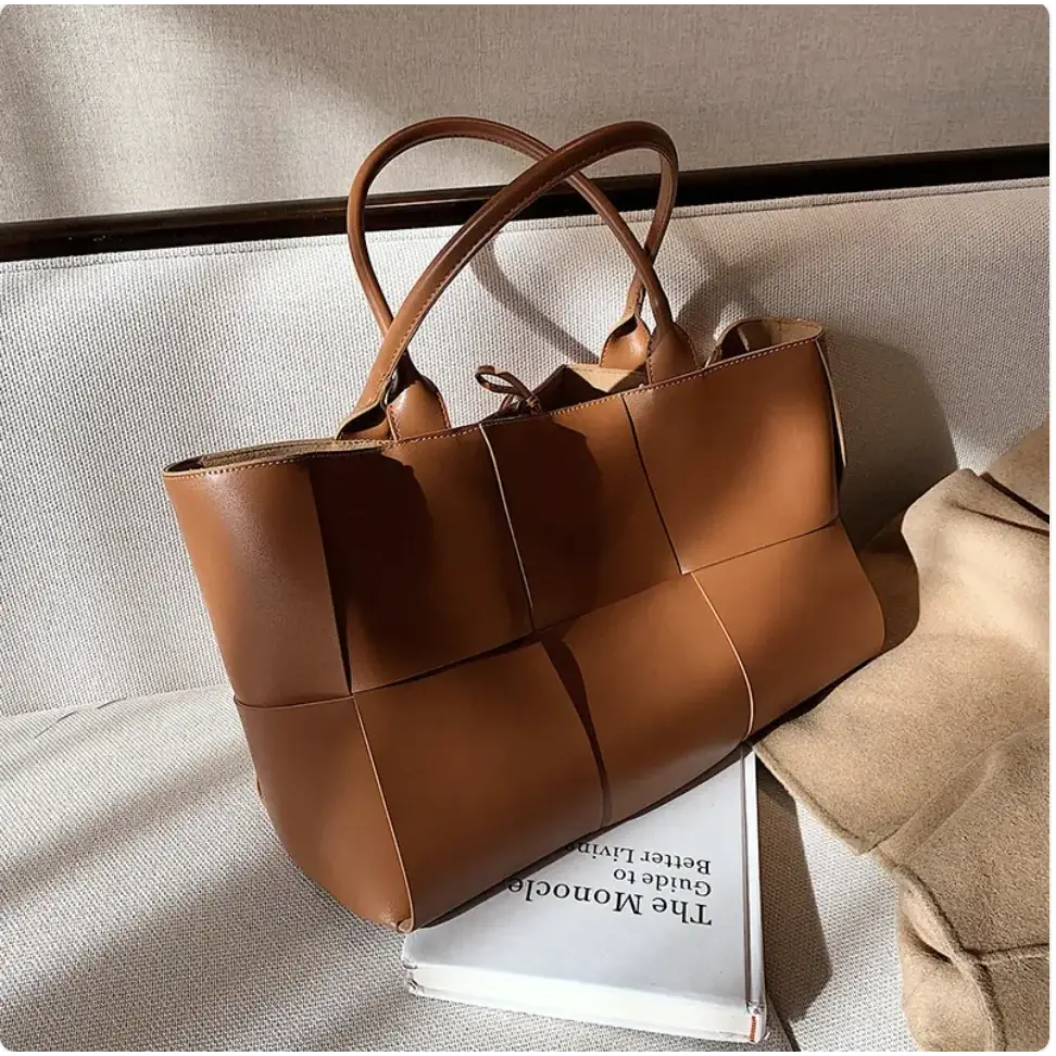 A tan leather tote bag with a woven, geometric panel design and matching handles.