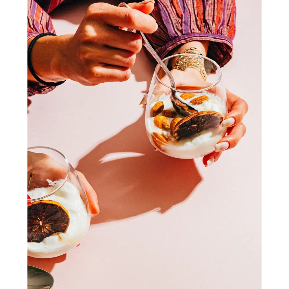 A clear glass dessert cup filled with creamy white yogurt, topped with sliced almonds and a dried orange slice.