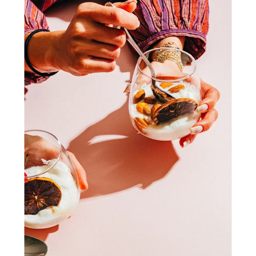 A clear glass dessert cup filled with creamy white yogurt, topped with sliced almonds and a dried orange slice.