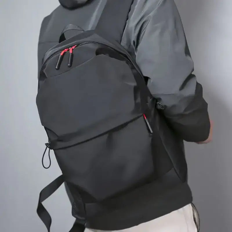 Black nylon backpack with red zipper pulls and a sleek, minimalist design.