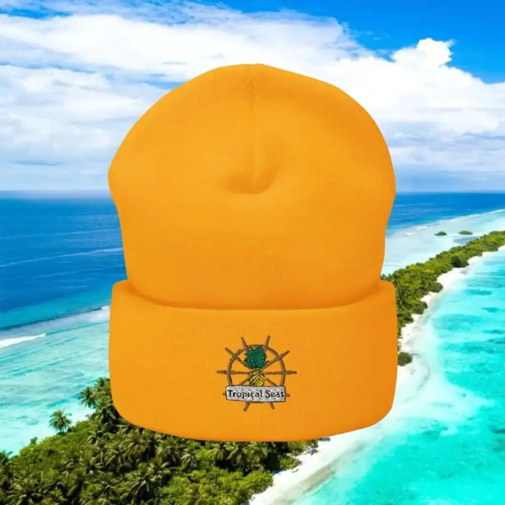 Bright orange knit beanie featuring a embroidered pineapple and ship wheel design with ’tropical seas’ text on the cuff.