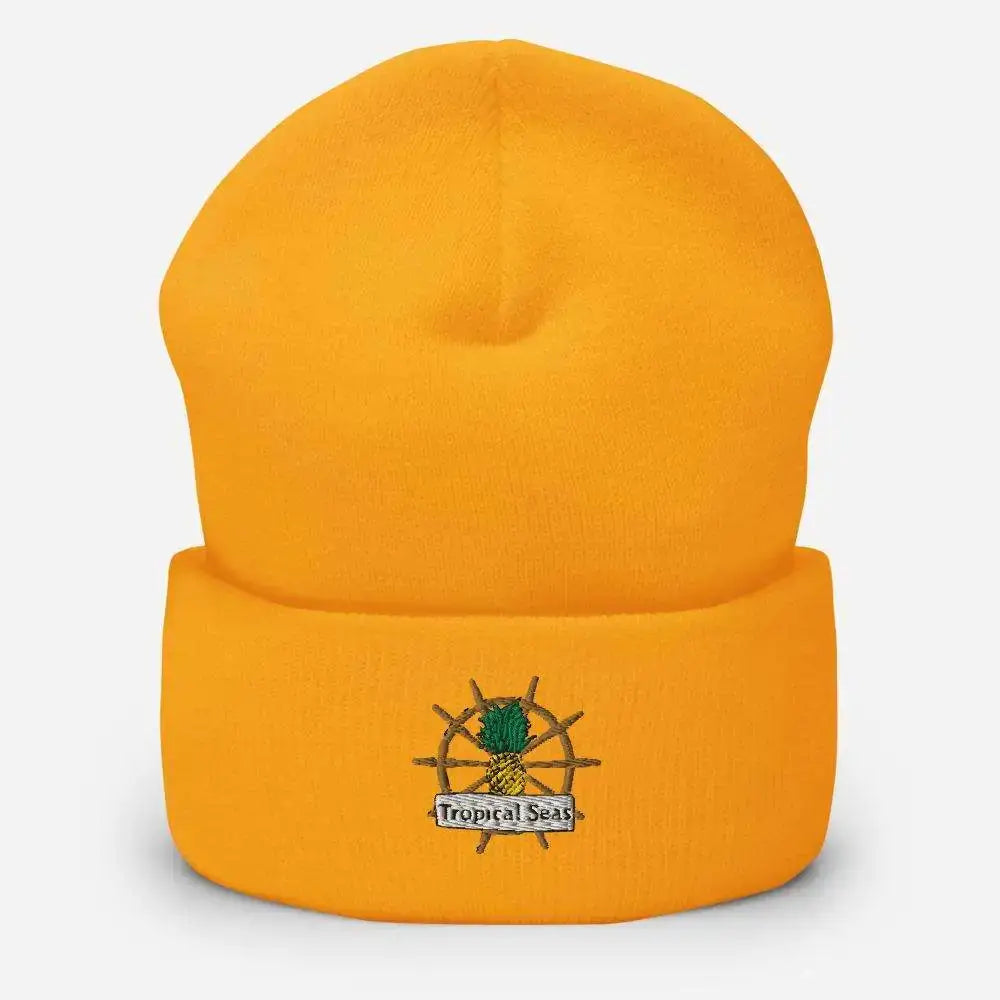 Bright orange knit beanie featuring an embroidered logo of a pineapple on a ship’s wheel with the text ’tropical seas’ beneath it.