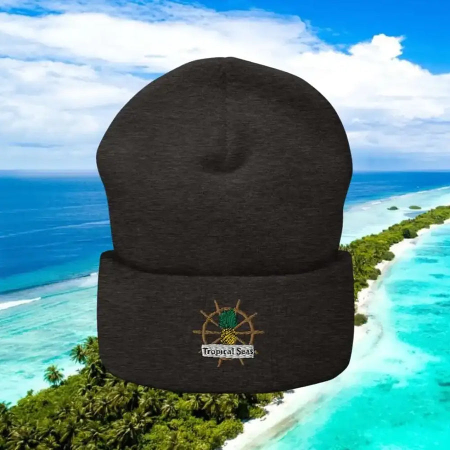 Dark gray knit beanie featuring an embroidered pineapple on a ship’s wheel with ’tropical seas’ text below.