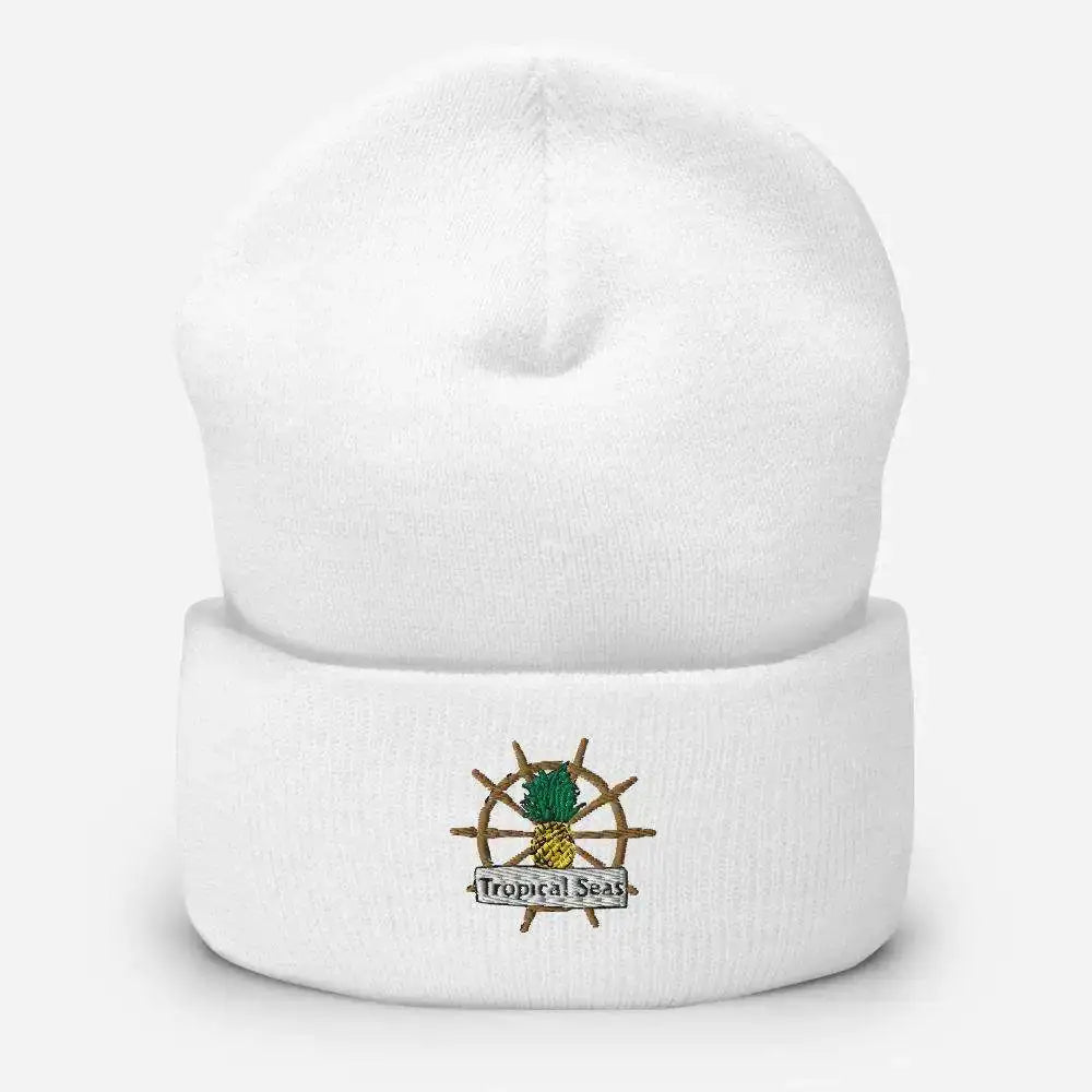 White knit beanie featuring an embroidered logo of a pineapple on a ship’s wheel with the text ’tropical seas’ beneath it.