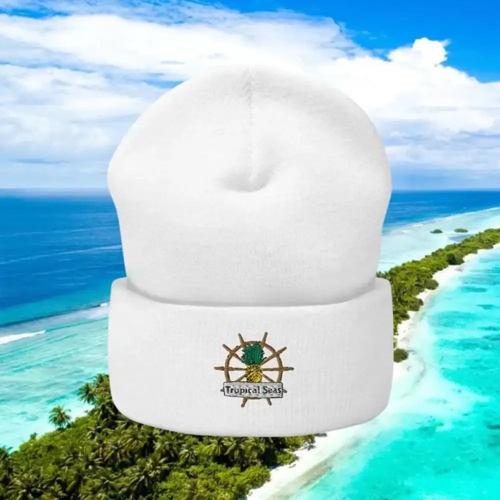 White knit beanie featuring a embroidered pineapple on a ship’s wheel with ’tropical seas’ text below.