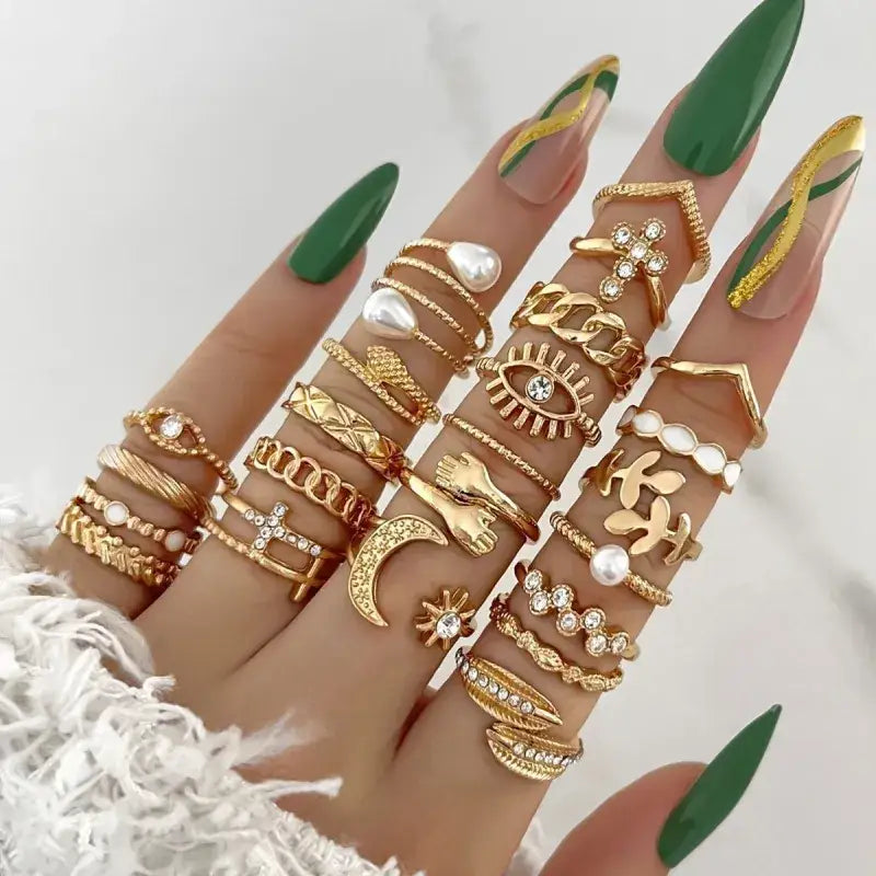 A hand adorned with multiple gold-toned rings featuring intricate designs, including charms like an eye, a crescent moon, and pearl accents.
