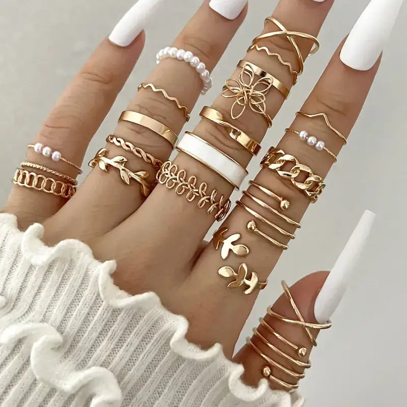 A hand adorned with multiple gold-toned rings featuring intricate designs including chains, leaves, flowers, and pearl accents.