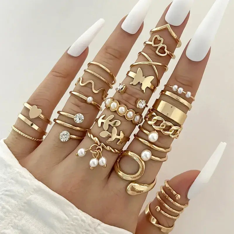 A hand adorned with multiple gold-toned rings featuring various designs including hearts, butterflies, pearls, and chains.