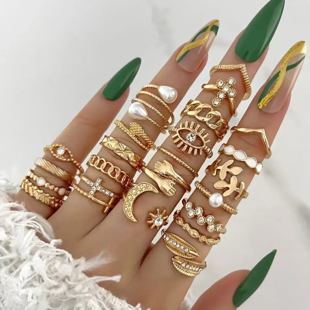 A hand adorned with multiple gold-toned rings featuring intricate designs, including an eye motif, a crescent moon, and pearl accents.