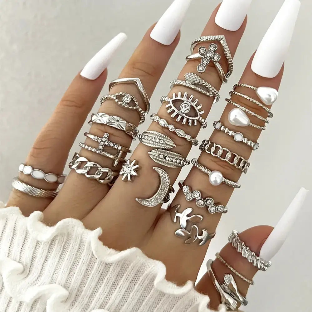 A hand adorned with numerous silver-toned rings featuring intricate designs like eyes, moons, stars, and pearls.