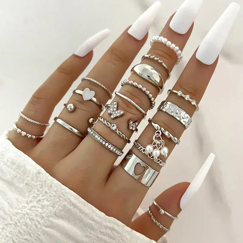 A hand adorned with multiple silver rings featuring various designs including hearts, butterflies, pearls, and geometric patterns.