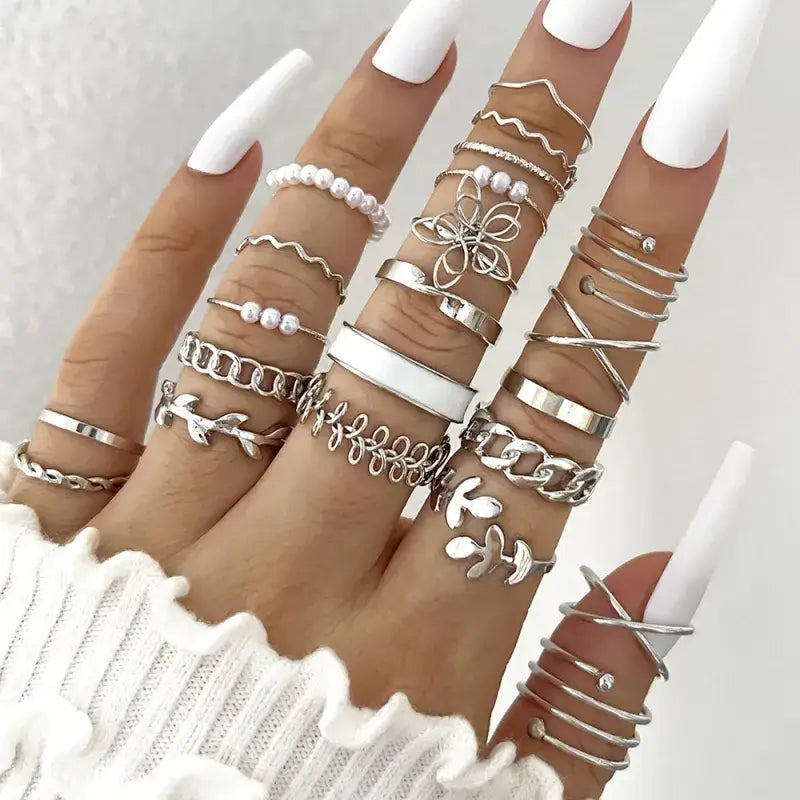 A hand adorned with multiple silver rings featuring intricate designs including chains, floral motifs, and pearl accents.