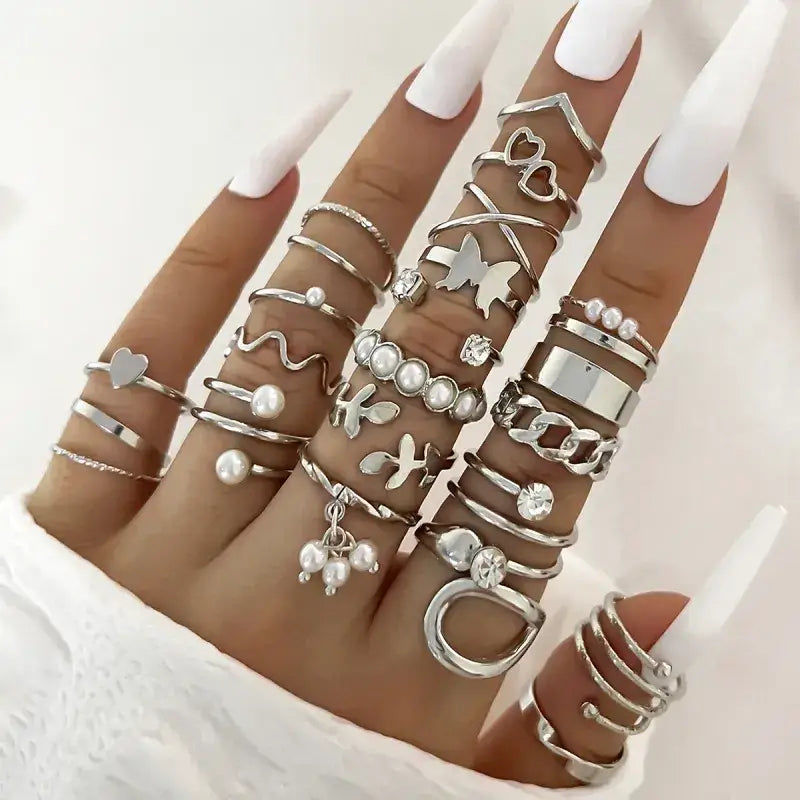 A hand adorned with a collection of silver-toned rings featuring various designs including hearts, butterflies, pearls, and geometric shapes.