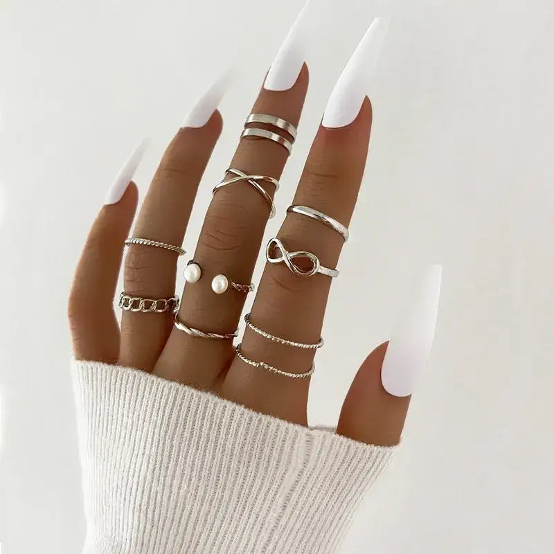 A hand adorned with multiple silver-toned rings, featuring various designs including infinity symbols and pearl accents.