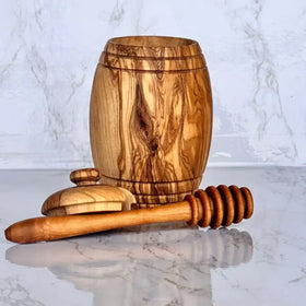 Handcrafted olive wood honey barrel with matching lid and dipper, featuring natural grain patterns and a warm golden-brown finish.