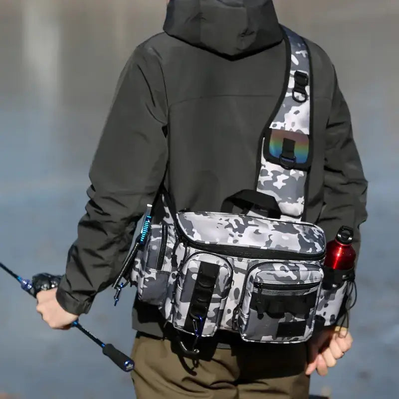 Gray and white camouflage fishing gear bag with multiple compartments, black straps, and a reflective patch on the shoulder strap.