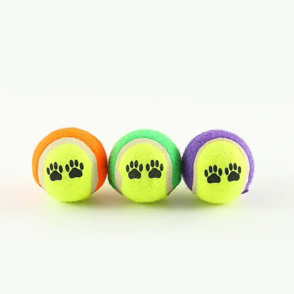 Three brightly colored tennis balls, each featuring a black paw print design on the yellow felt surface.