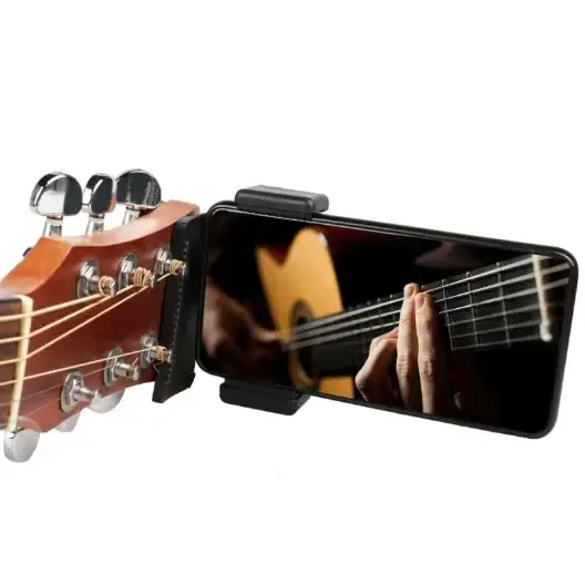 Black smartphone mounted on a guitar headstock clamp, displaying an image of hands playing a classical guitar.