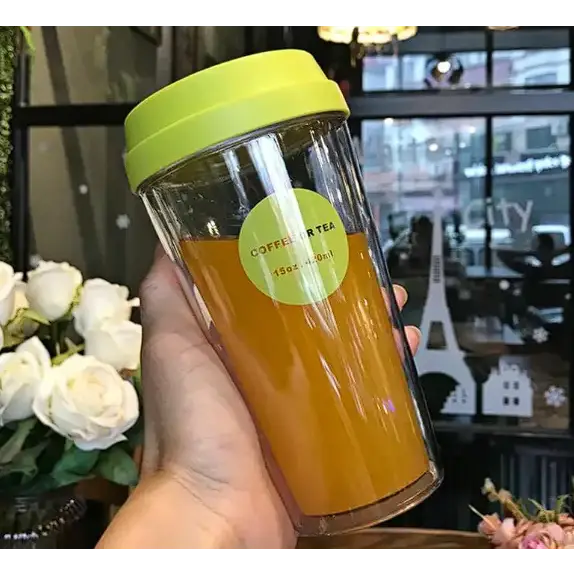 A clear double-walled tumbler with a bright lime green lid and matching circular label, filled with orange liquid.