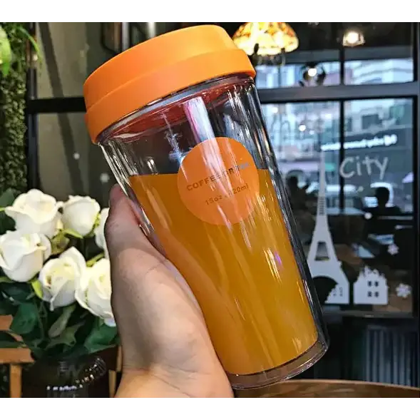 Orange lided transparent double-walled travel mug filled with orange juice.