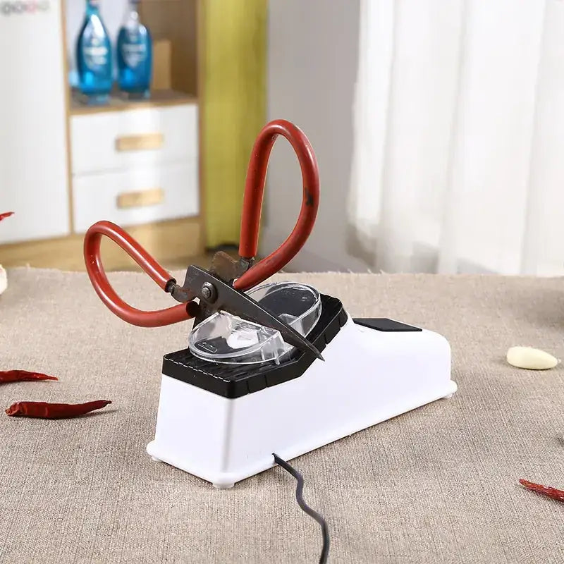 Red-handled scissors resting on a white and black electric knife sharpener.
