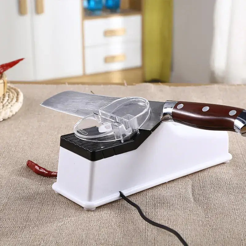 White and black electric knife sharpener with transparent protective cover holding a wooden-handled kitchen knife.