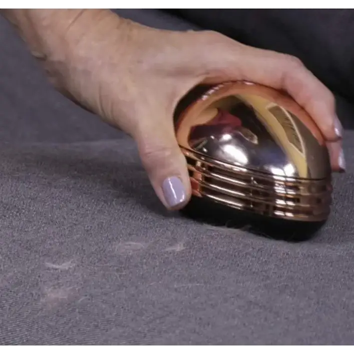 A sleek, rose gold-finished lint roller with a smooth, rounded top and concentric ridges along its side.