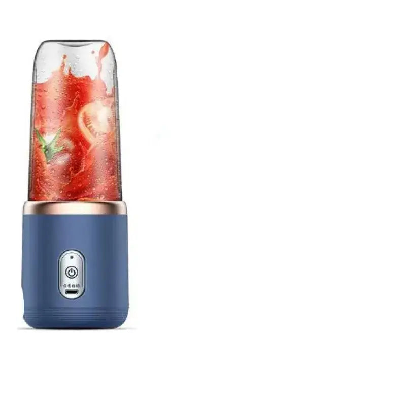Blue handheld blender with a clear glass blending cup filled with red tomato juice and green herbs, featuring a rose gold accent ring around the base.