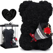 Black rose-covered teddy bear with a single red rose bouquet tucked into its side.