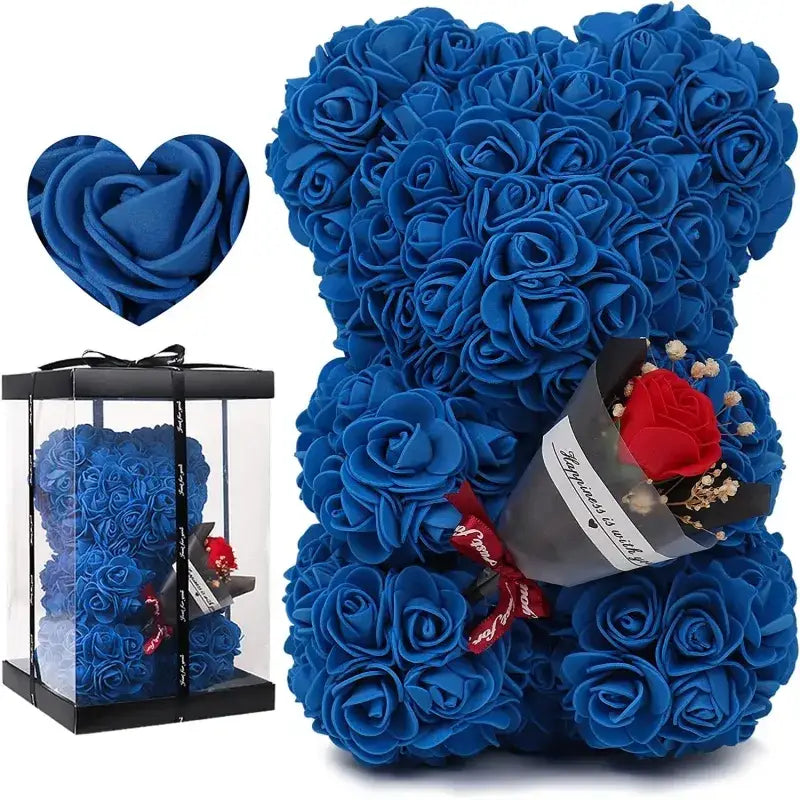 A plush blue rose-covered bear with a single red rose nestled in its arm, presented alongside its clear gift box.