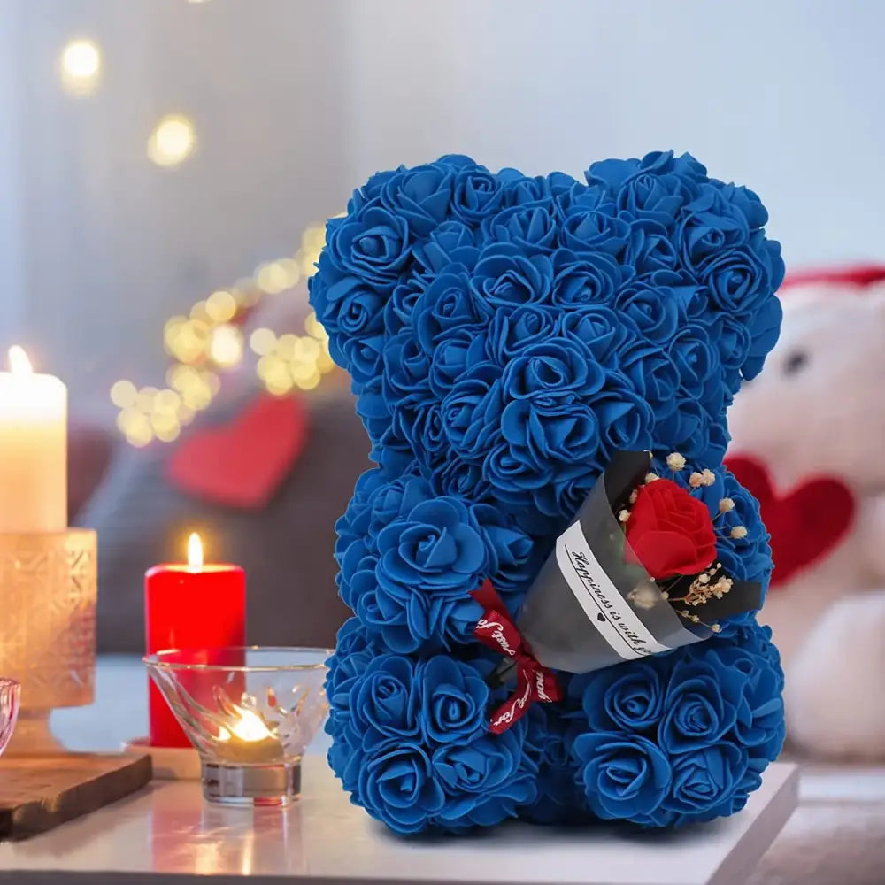 A plush blue teddy bear crafted entirely from artificial roses, holding a small bouquet of red and white flowers in its paw.