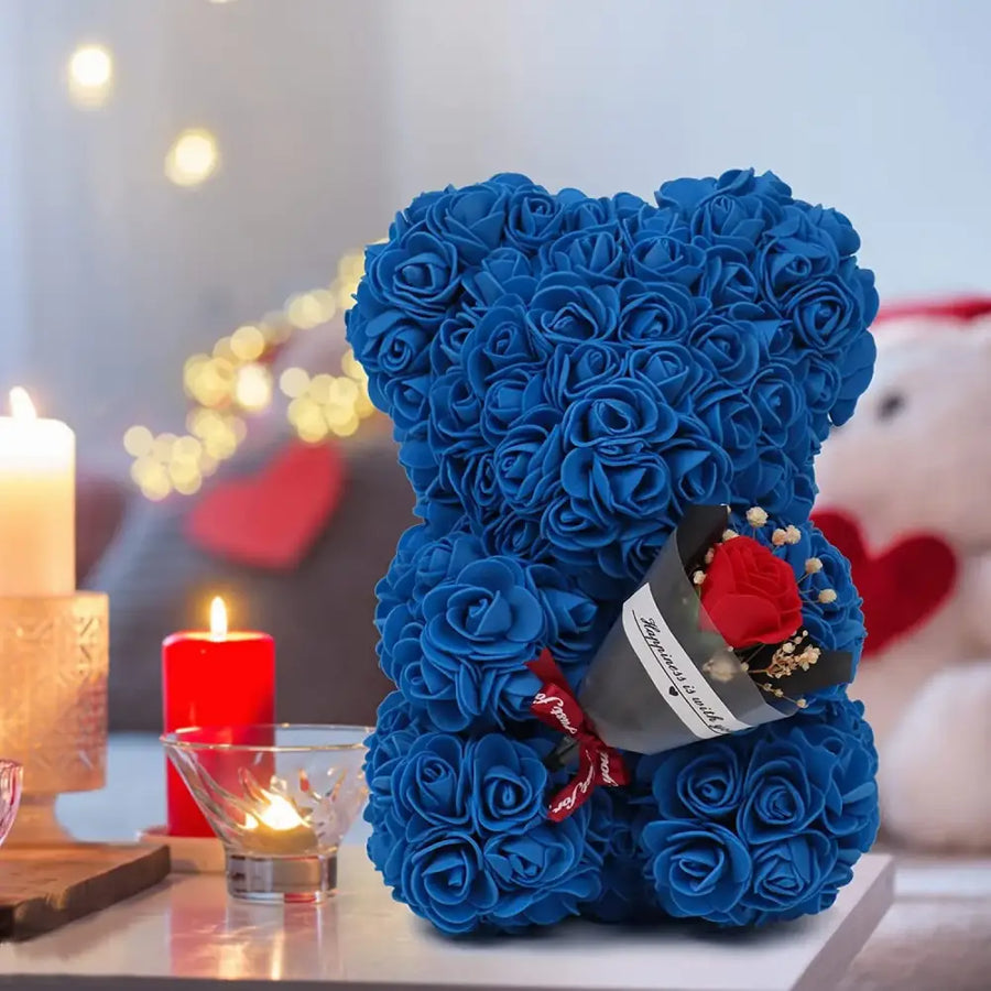 A plush blue teddy bear crafted entirely from artificial roses, holding a small bouquet of red and white flowers in its paw.