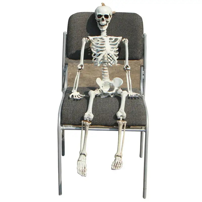 White plastic skeleton figurine seated on a metal-framed chair with dark gray upholstered seat and backrest.